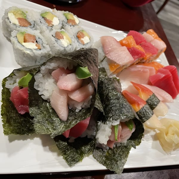 A white platter filled with various sushi rolls, hand rolls, and sashimi from Sushi Palace.