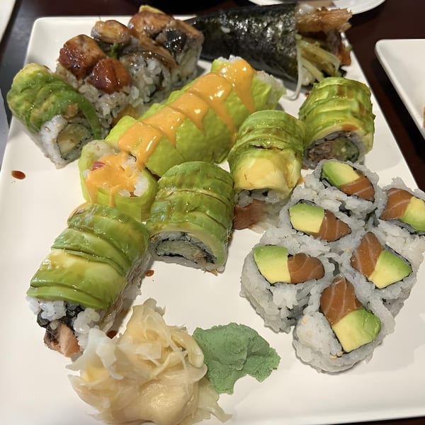 A white platter filled with various sushi rolls, including avocado-topped and salmon-avocado rolls, with ginger and wasabi.