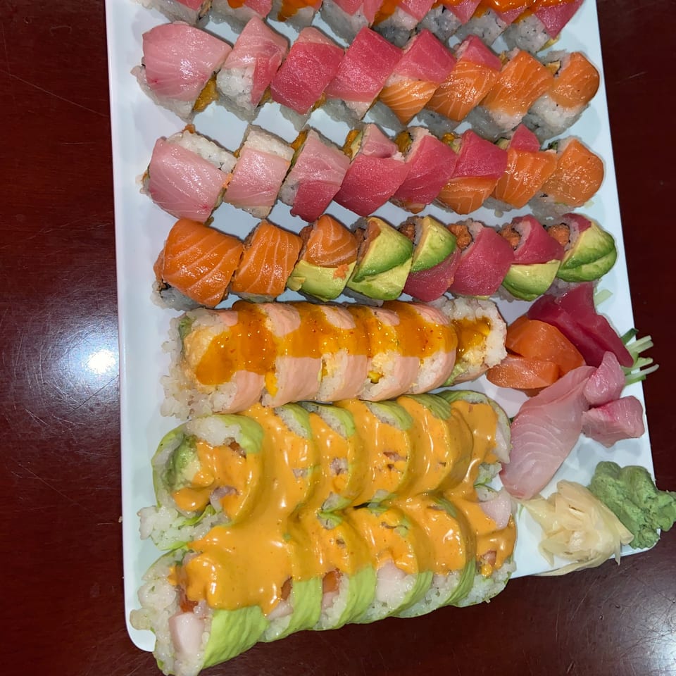 A large white platter filled with various colorful sushi rolls, sashimi, and garnishes.