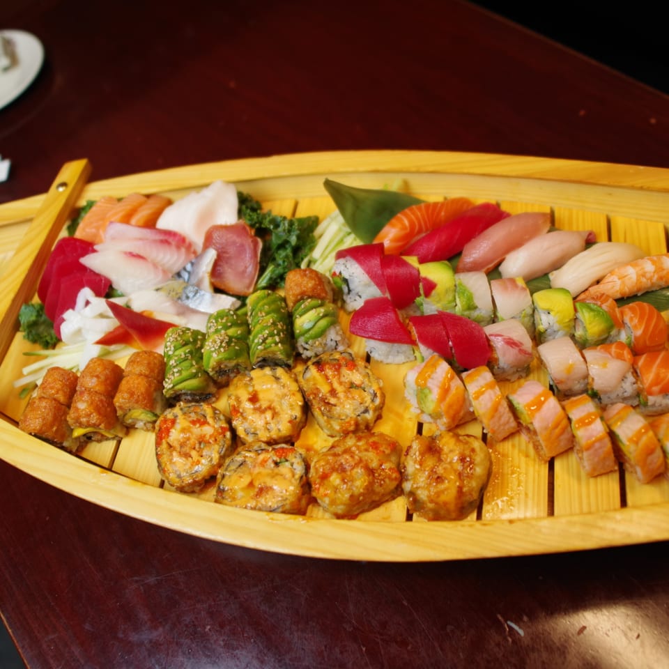 A large wooden boat filled with various colorful sushi, sashimi, and rolls on a dark table.