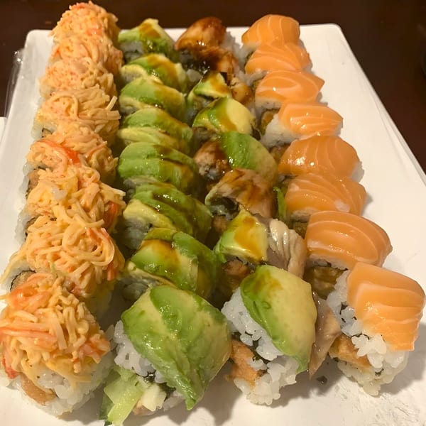 A white platter holds three rows of Sushi Palace sushi rolls: spicy crab, avocado, and salmon.
