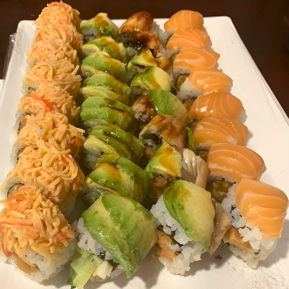 A white platter holds three rows of Sushi Palace sushi rolls: spicy crab, avocado, and salmon.