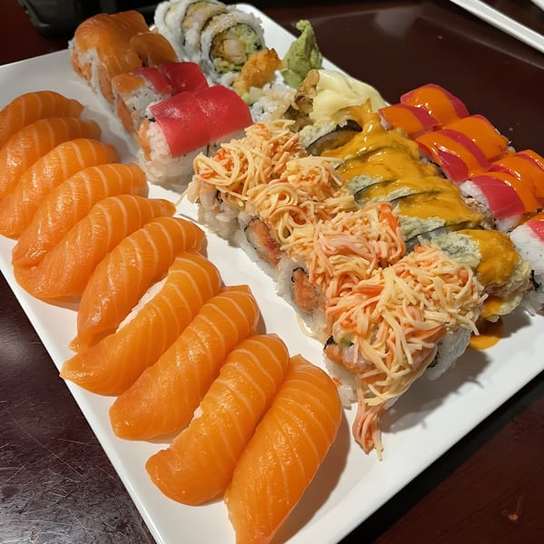 A large white platter filled with various colorful sushi rolls and salmon nigiri from Sushi Palace.