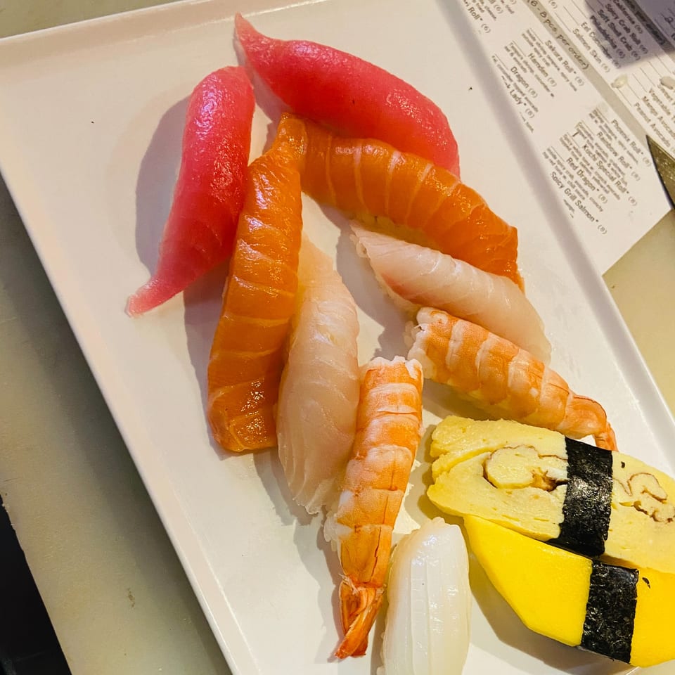A white plate holds a colorful assortment of Sushi Palace nigiri, including tuna, salmon, shrimp, and tamago.