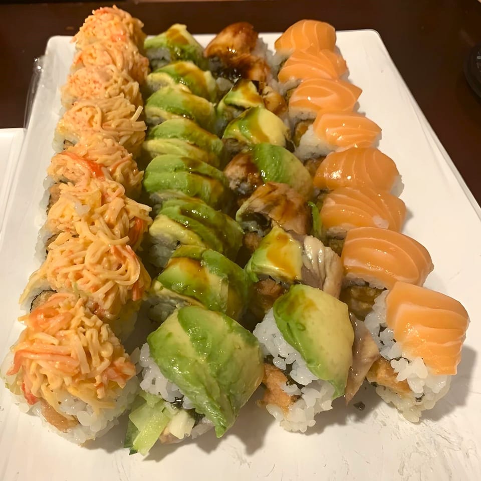 A white platter filled with three rows of various Sushi Palace sushi rolls, including salmon and avocado.