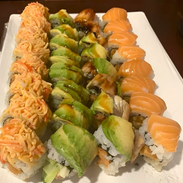 A white platter filled with three rows of colorful sushi rolls, including salmon, avocado, and crab.