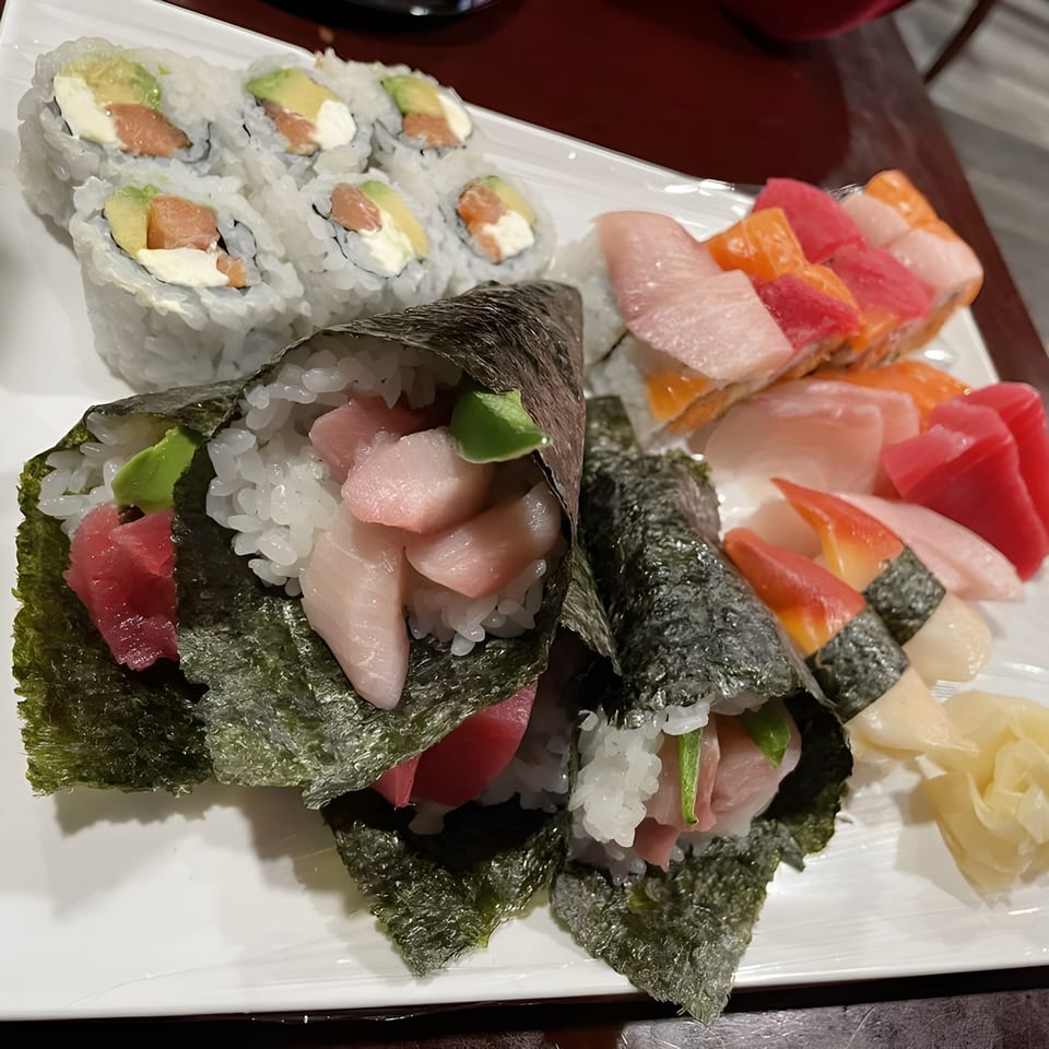 A white platter filled with various Sushi Palace sushi rolls, hand rolls, and sashimi.
